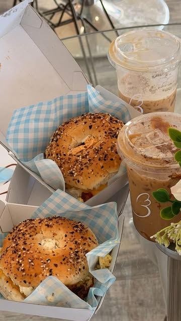 Two everything bagel sandwiches in take-out boxes with two iced coffees marked with the Baglory heart.